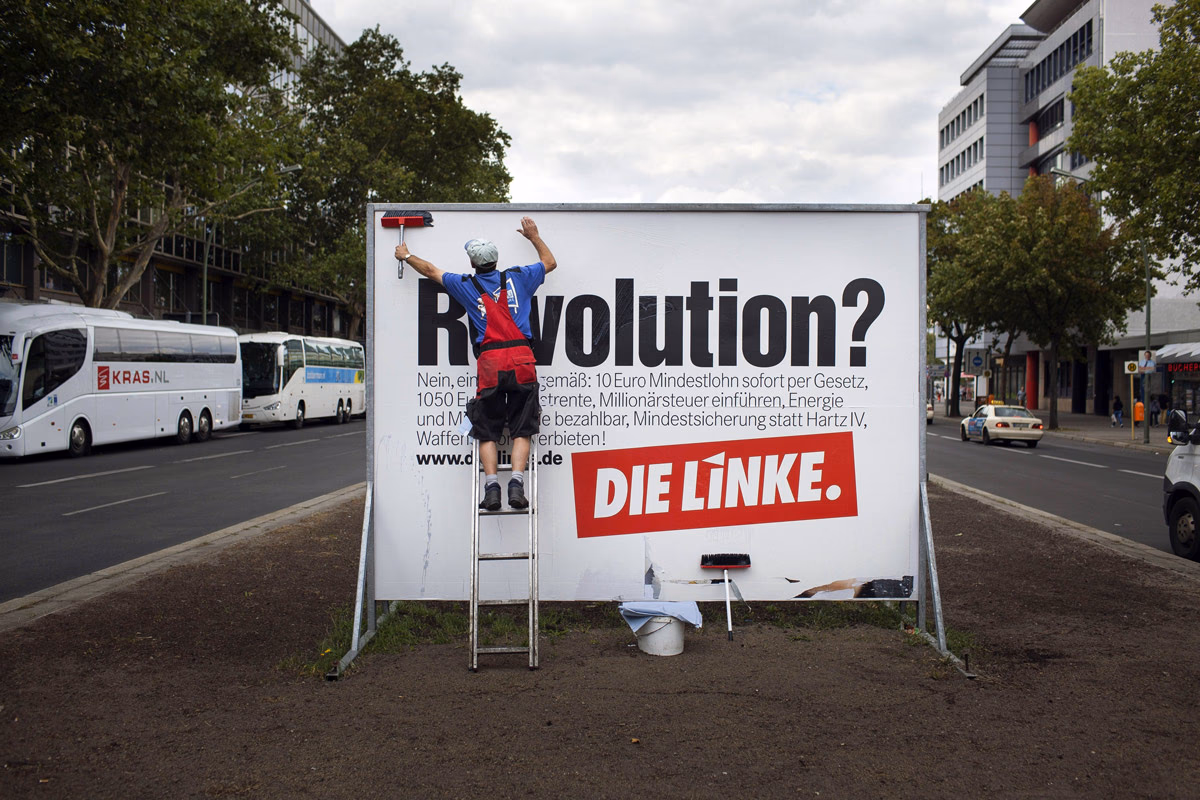 Ein Plakatkleber vor einem Wahlkampfplakat der Linken, aufgenommen im August 2013 in Berlin